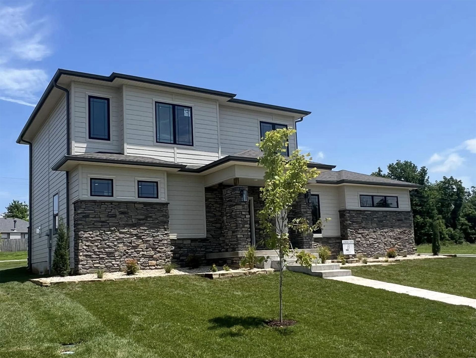 A modern two-story suburban house with light-colored siding and a stone facade under a clear blue sky.