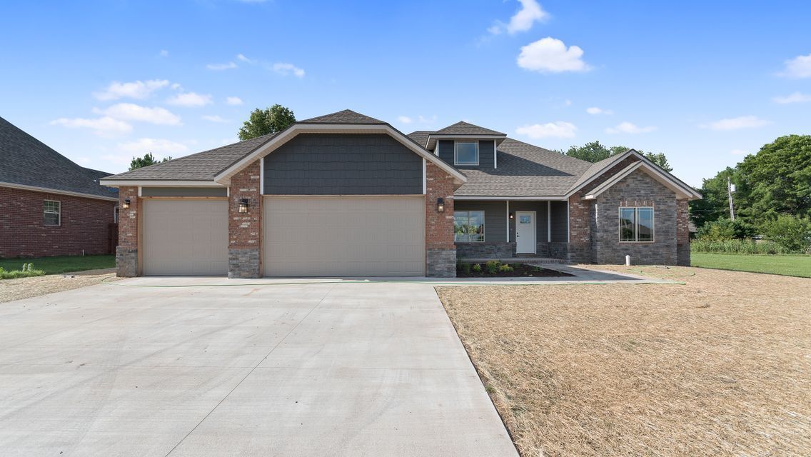 A tan, single-story house with a brick and gray siding facade, three-car garage, and a large concrete driveway.