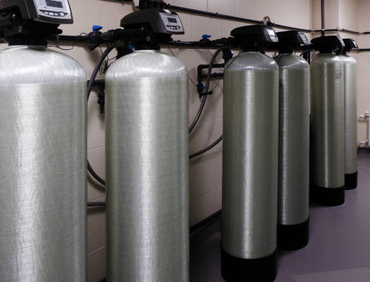 A row of tall, cylindrical water filtration tanks in an industrial setting.