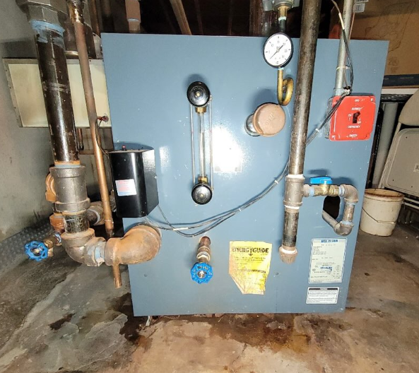 A blue, industrial-looking furnace in a basement setting, with pipes and gauges attached.