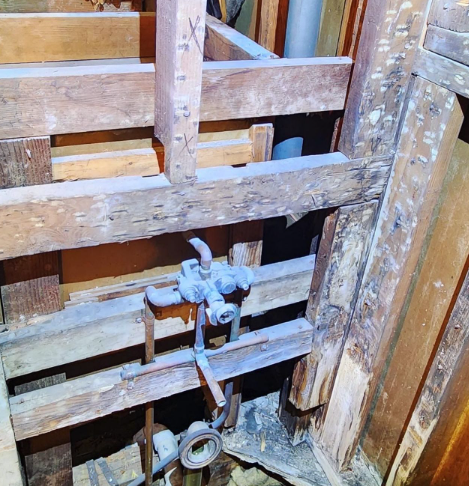 Bathroom plumbing, exposed in a wooden framework. Pipes and fixtures visible, wooden beams.
