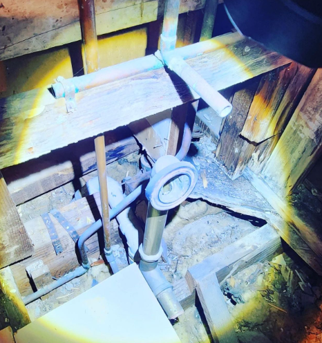 Plumbing pipes inside a wall cavity, wood beams, copper pipes, and a shower fixture.