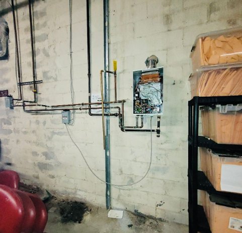 Copper pipes, a wall-mounted water heater, and shelving with boxes in a basement setting.