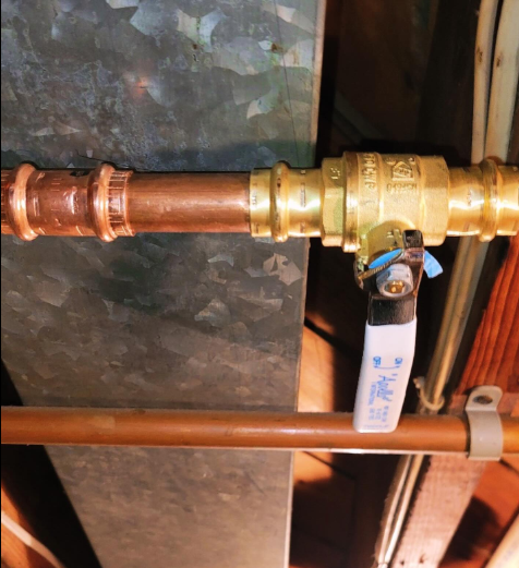 Copper pipes with brass valve. Metal ductwork and wood beams in background.