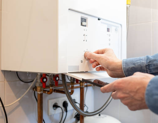 Person adjusts a dial on a white wall-mounted boiler with copper pipes; indoor setting.