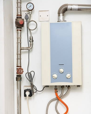 A white and blue water heater on a wall, connected to pipes and gas lines.