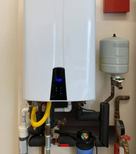 White tankless water heater with black digital display and plumbing on a wall.