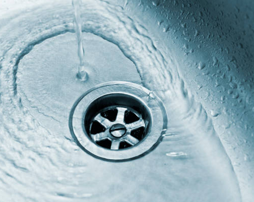 Water flowing into a sink drain. Shiny, metallic drain surrounded by swirling water.