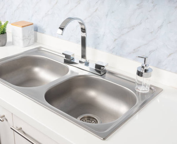 Stainless steel double sink with chrome faucet and soap dispenser on a white countertop.