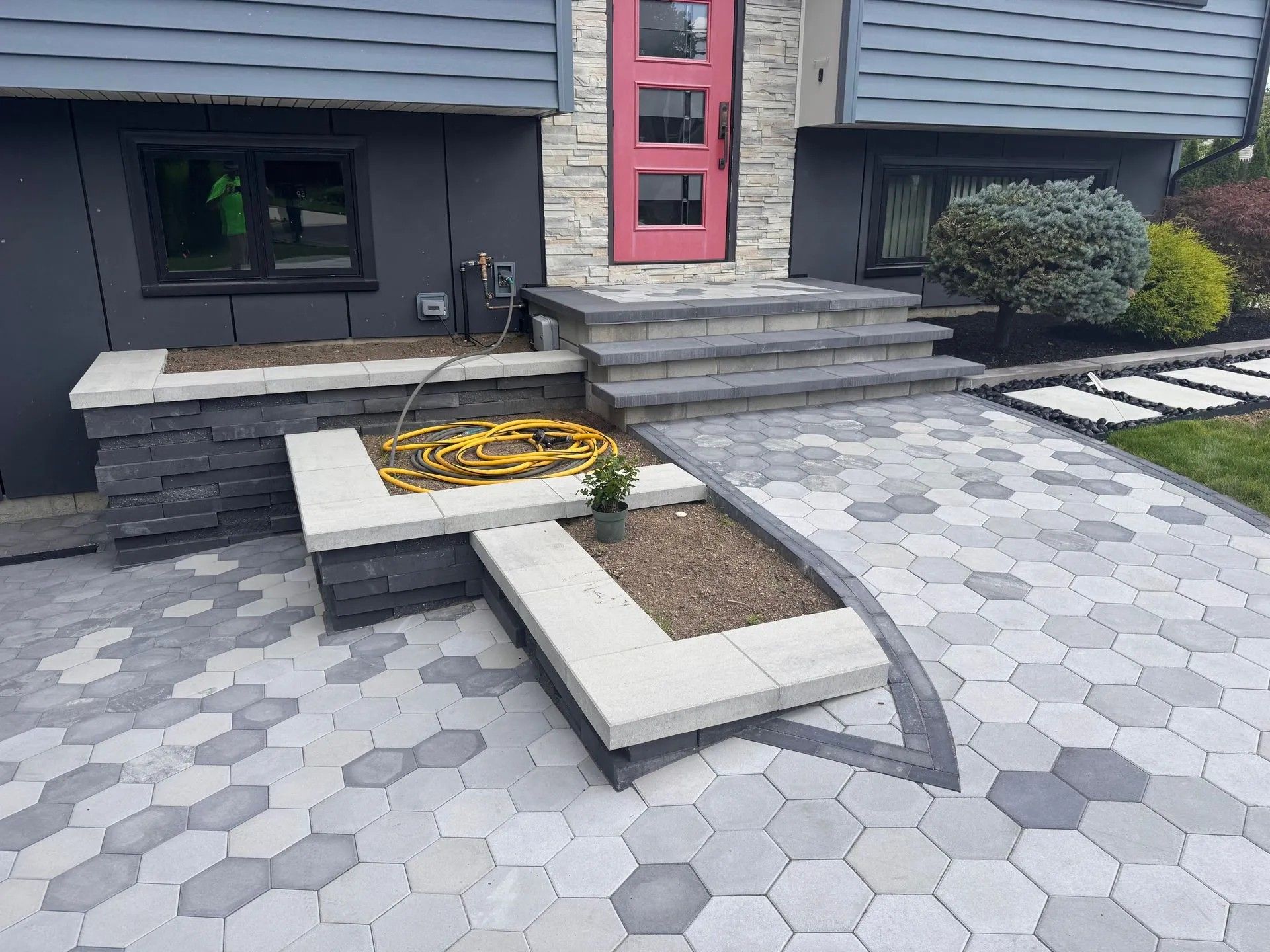 Modern front entry with stone steps, hex paver walkway, and a built-in planter bed by a red door.