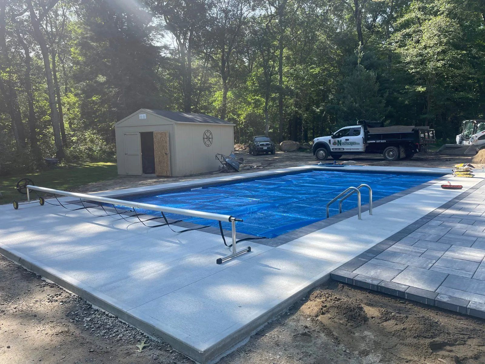 Covered backyard swimming pool under construction with blue liner, concrete deck, shed, and parked truck nearby.