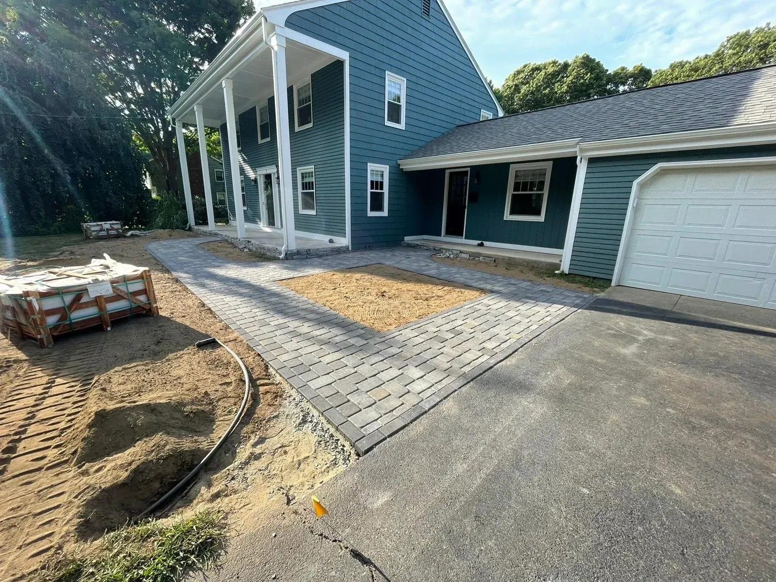 Blue house with a white garage, paved driveway, and landscaped front yard under construction.