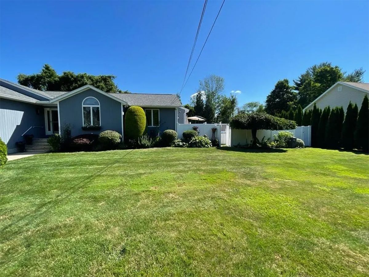 Suburban house with a large green lawn, shrubs, and a clear blue sky.