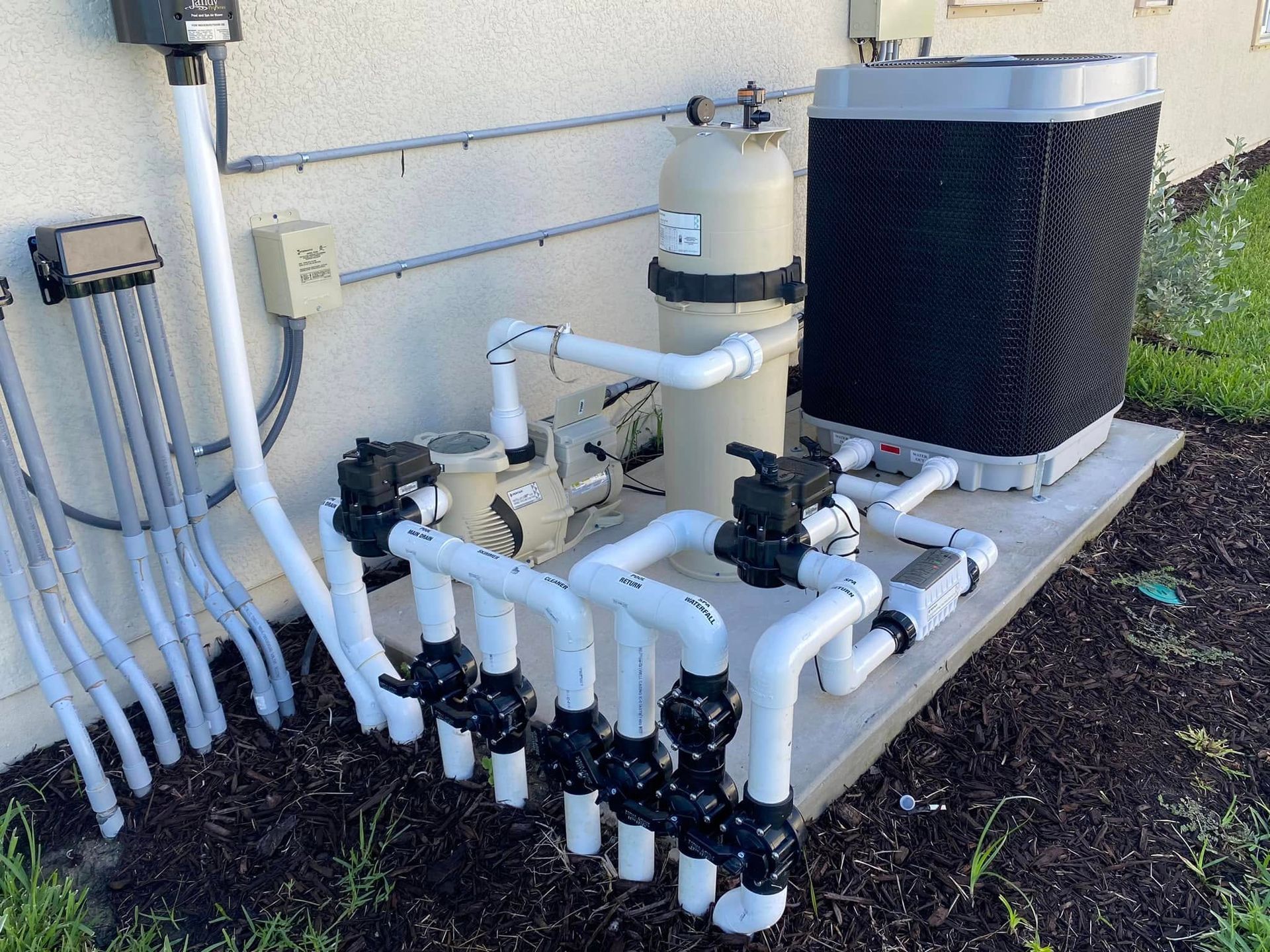 Outdoor HVAC or water filtration equipment with white pipes and black tanks beside a building