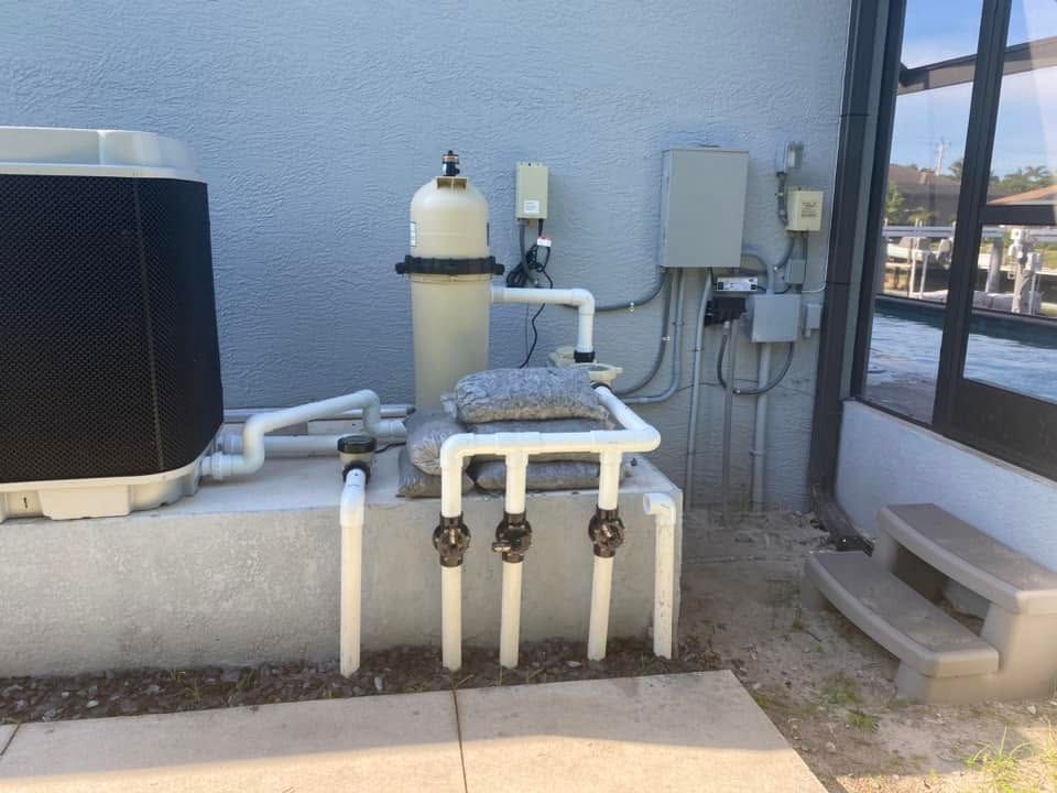 Outdoor utility equipment with pipes, valves, and a tank beside a building wall and window.