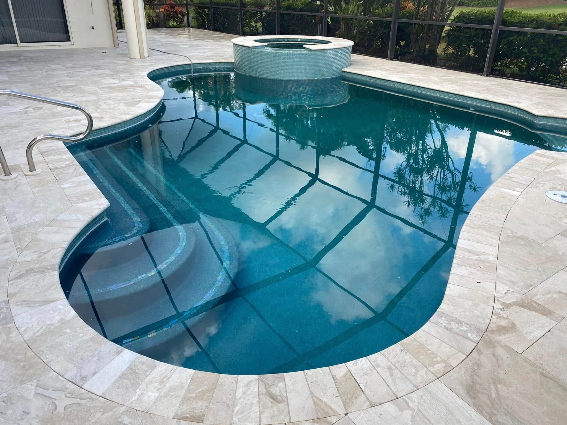 Curved backyard swimming pool with blue water, white stone deck, and a raised spa waterfall.