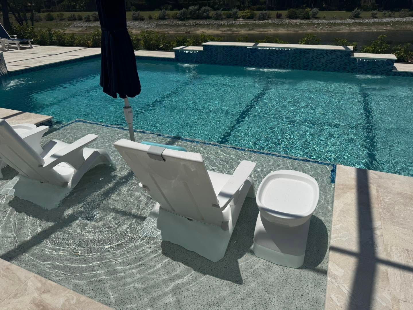 Poolside lounge chairs beside a turquoise swimming pool with a closed black umbrella.