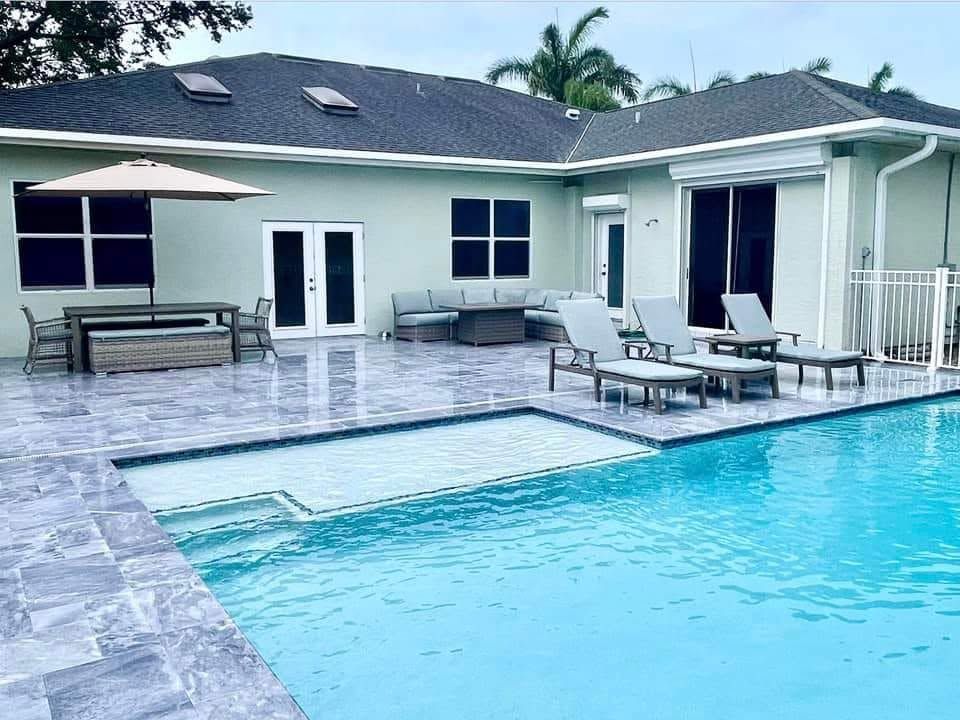 Backyard patio with a swimming pool, lounge chairs, umbrella, and a house with sliding glass doors.