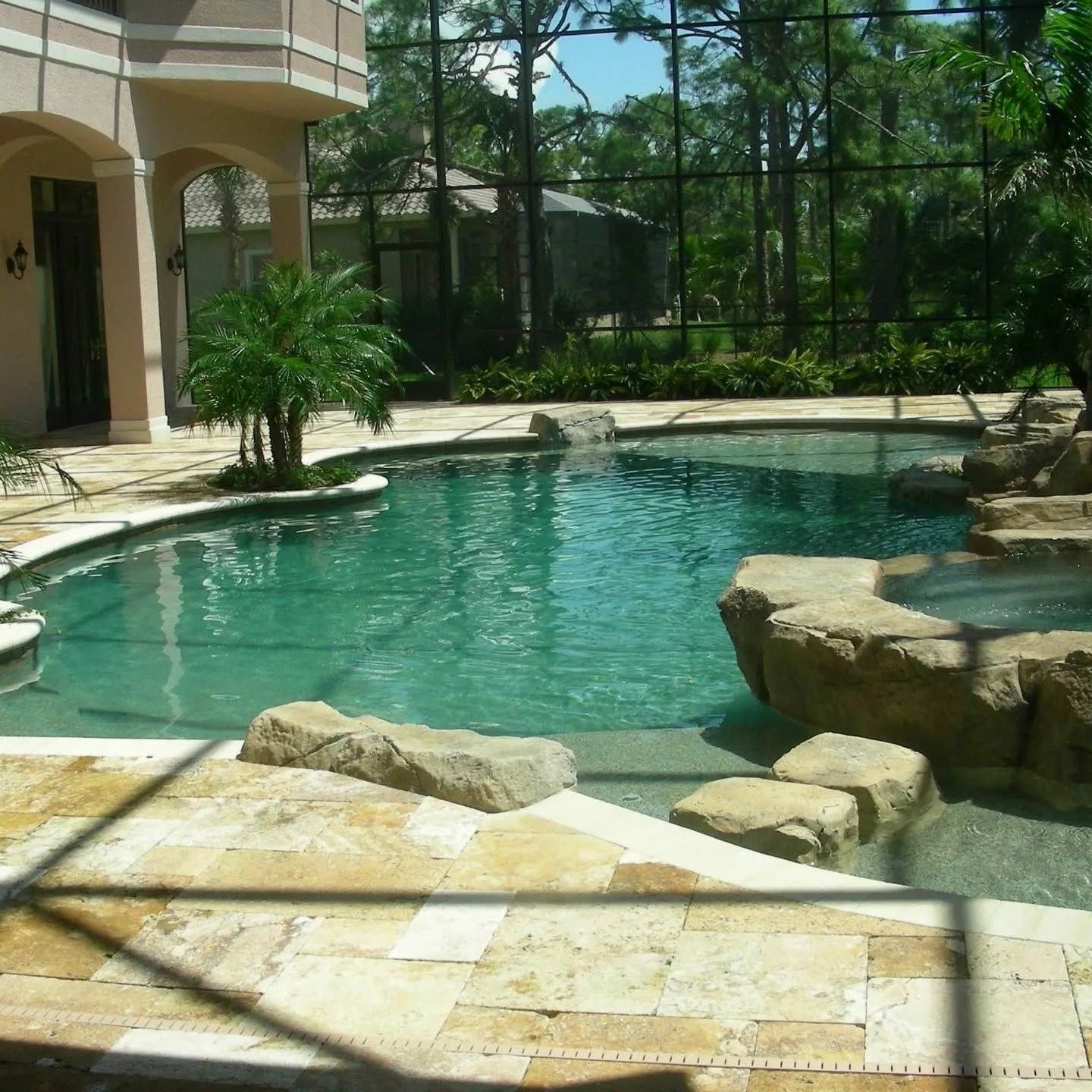 Backyard swimming pool with turquoise water, stone edging, and a screened patio area.