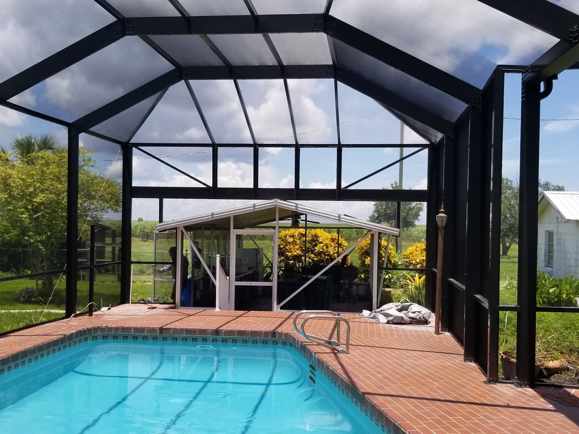 Screened-in pool enclosure over a backyard swimming pool with brick deck and cloudy sky overhead