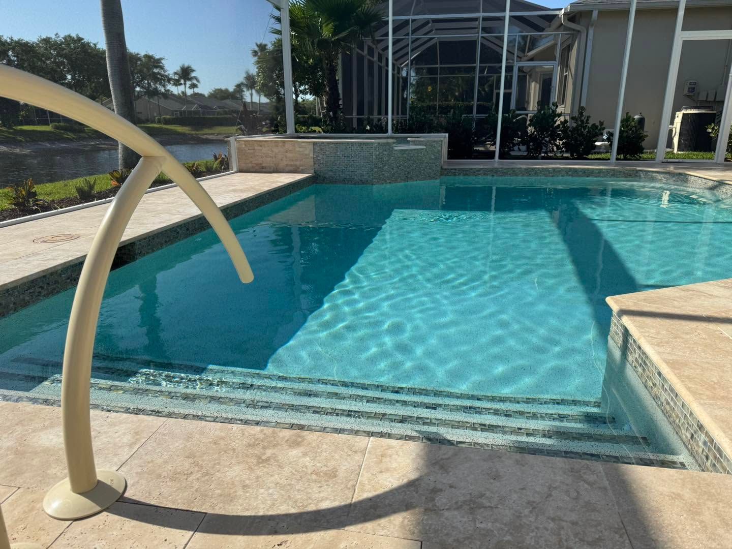 Outdoor swimming pool with a beige handrail and steps leading into clear blue water возле modern building