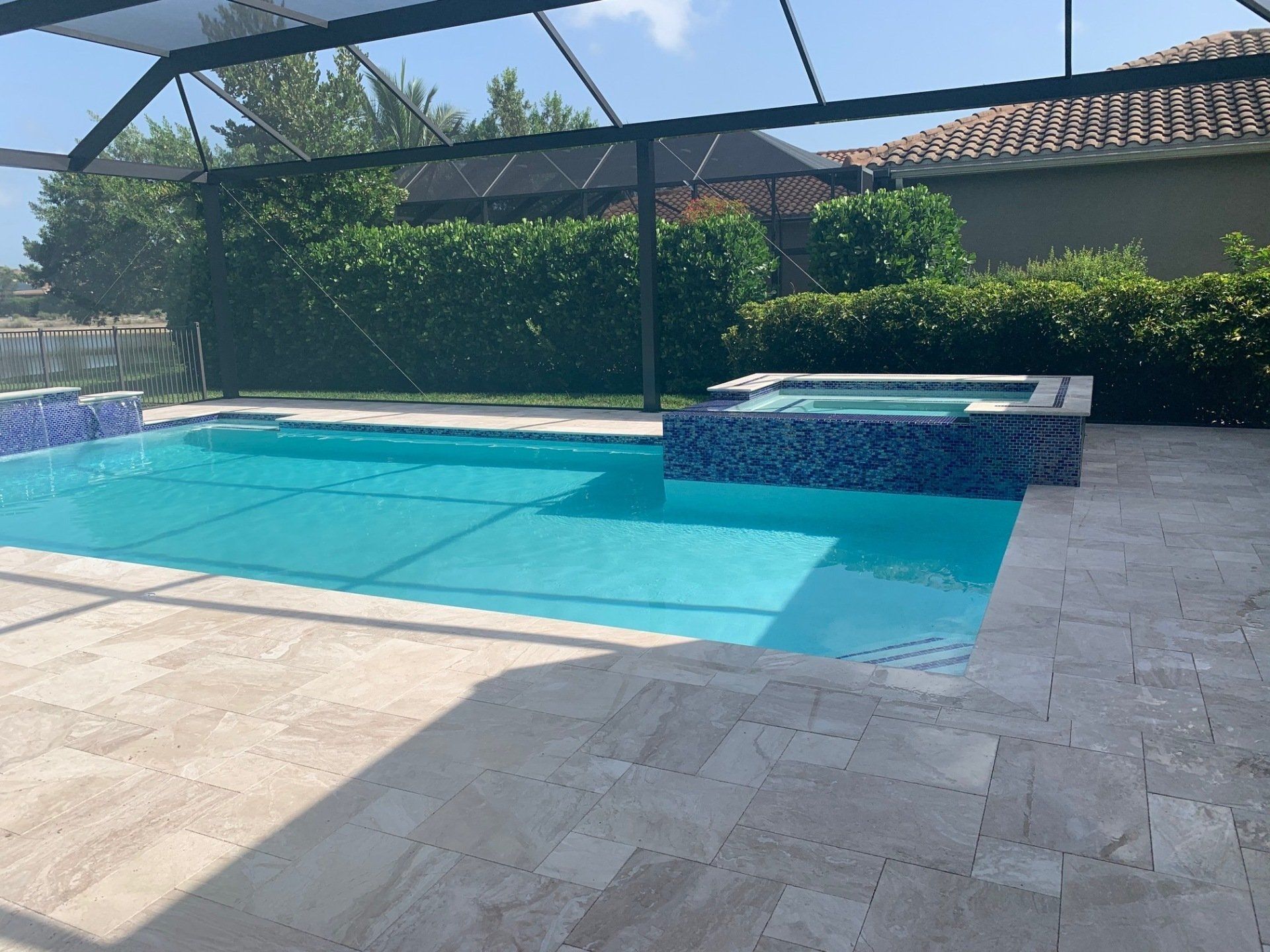Backyard pool with turquoise water, stone patio, and a screened enclosure beside a spa.