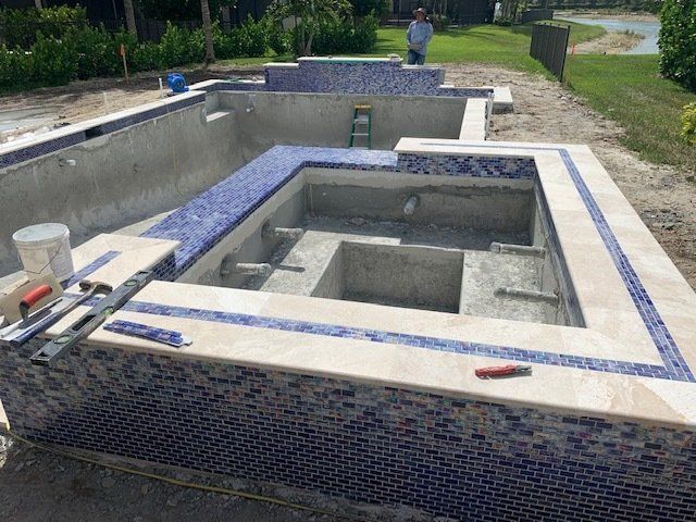 Partially tiled backyard pool under construction with concrete basins and tools nearby