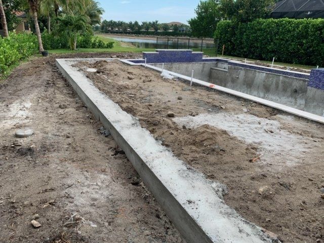 Concrete-lined garden pool or pond under construction beside a path, with bare soil and greenery nearby