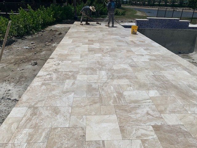 Workers installing light stone pavers on a long outdoor patio walkway