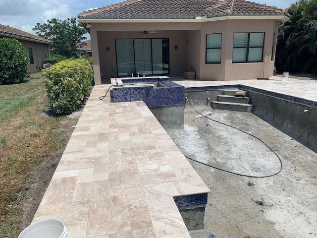 Backyard pool under construction beside a patio and house with stone pavers and unfinished concrete basin