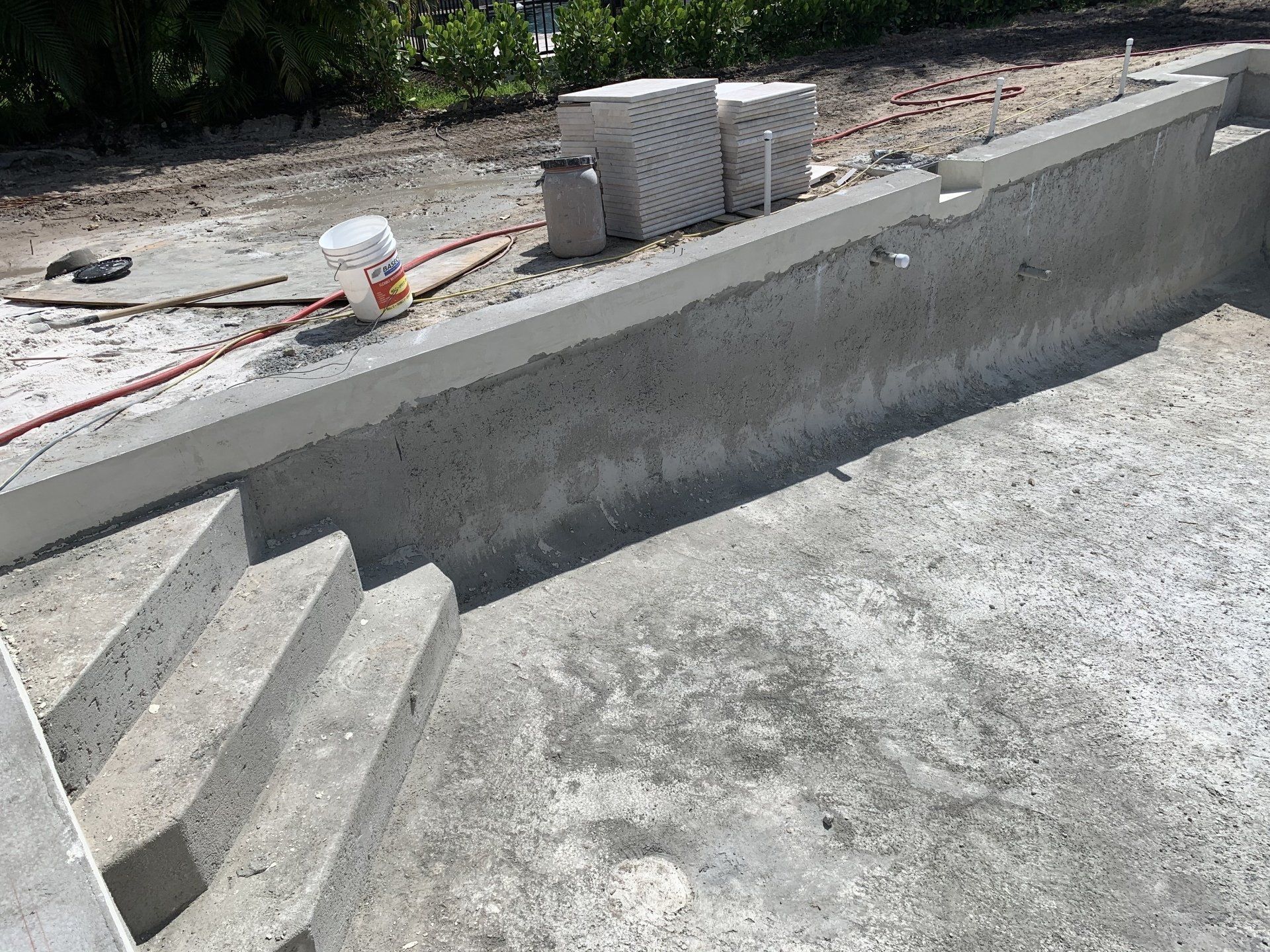 Concrete swimming pool under construction with steps, unfinished walls, and building materials on top