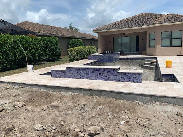Backyard patio with a tiered blue-tiled pool and concrete deck beside a house under construction