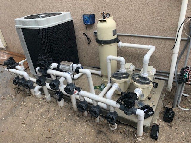 Pool equipment with pipes, valves, and filters beside a house exterior.