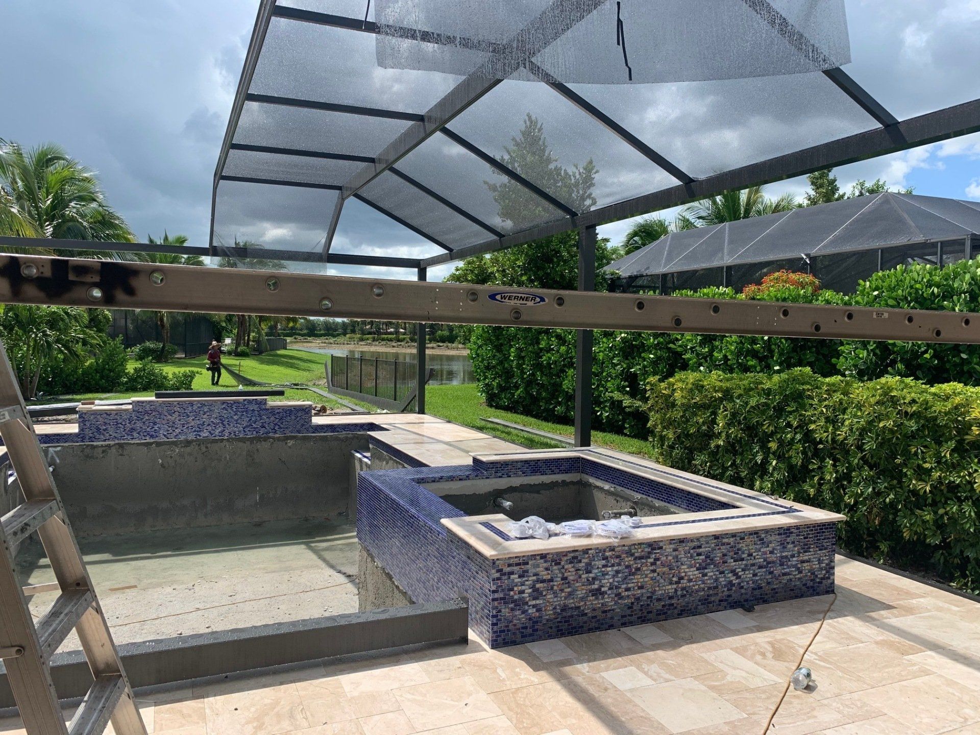 Outdoor patio with two tiled fire pits, a pergola roof, and green hedges in the background
