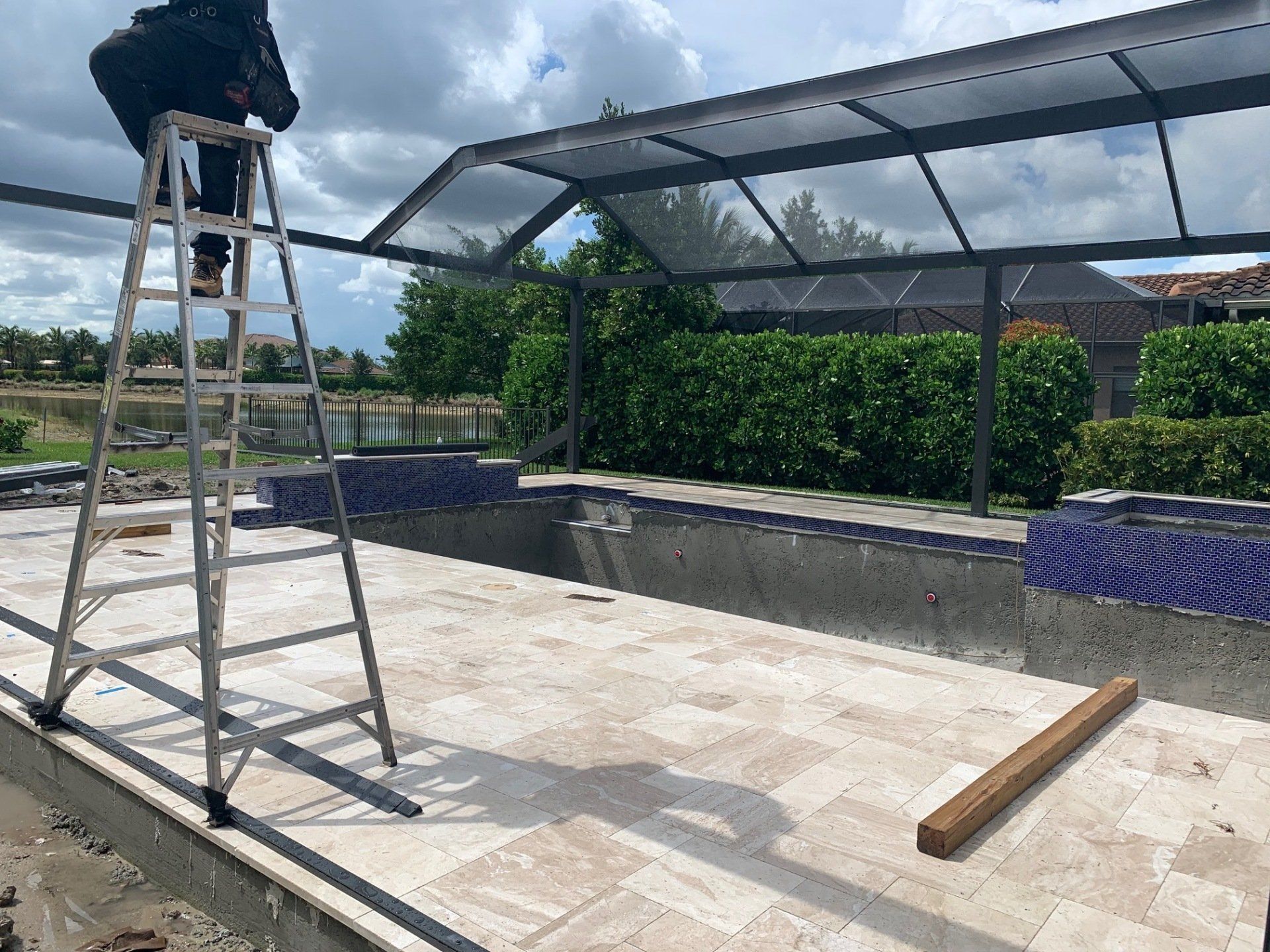 Person on a ladder installing a metal roof frame over a rooftop patio under a cloudy sky