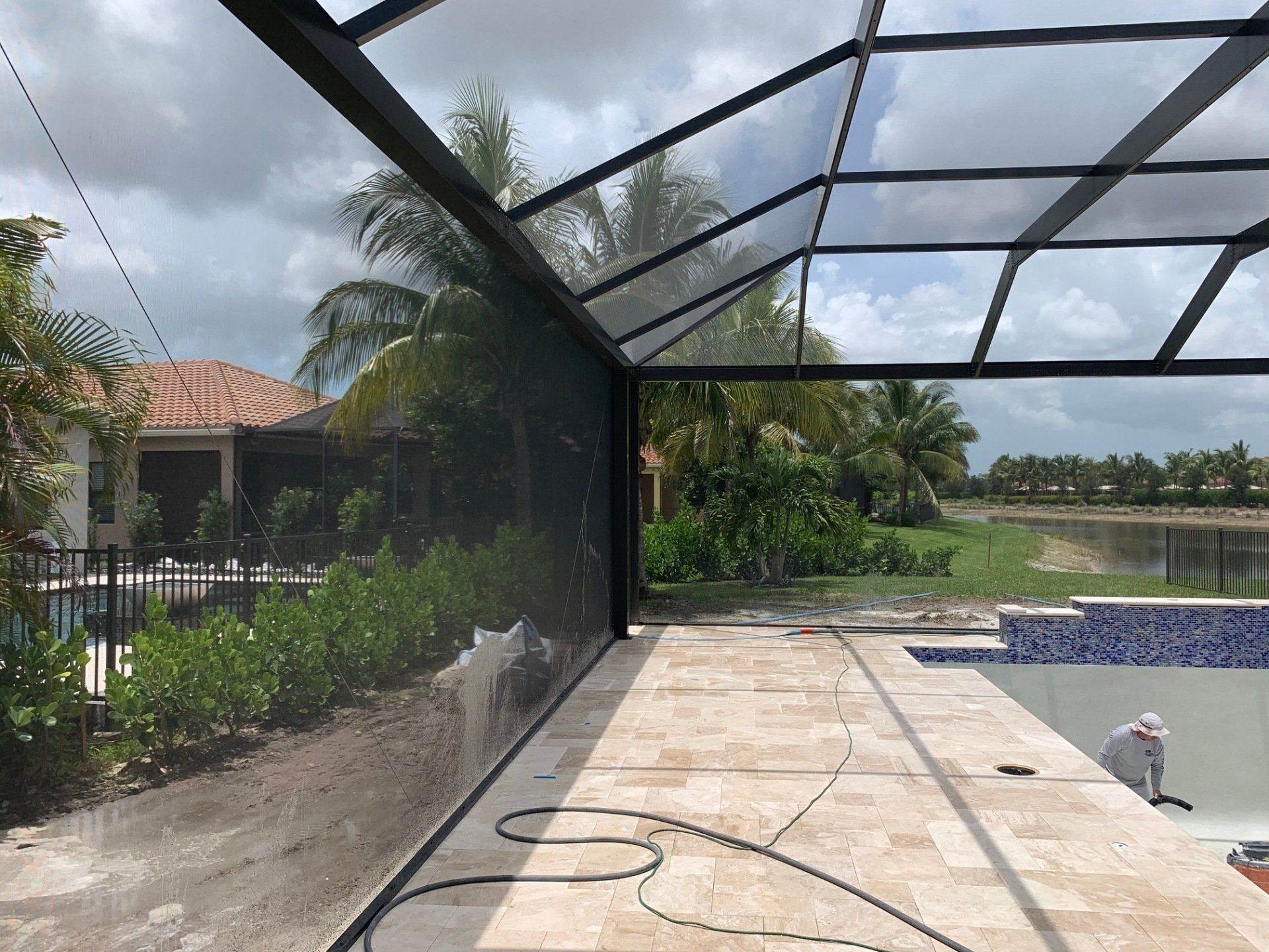 Screened pool patio with tiled deck, pool, palm trees, and a house in the background