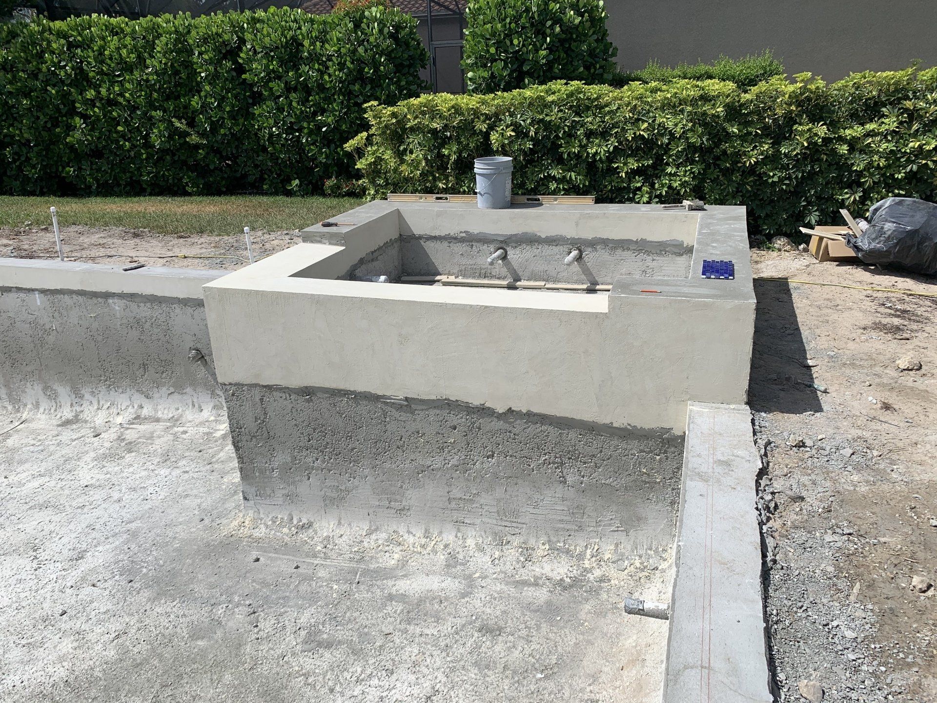 Concrete utility sink under construction beside a hedge and gravel area