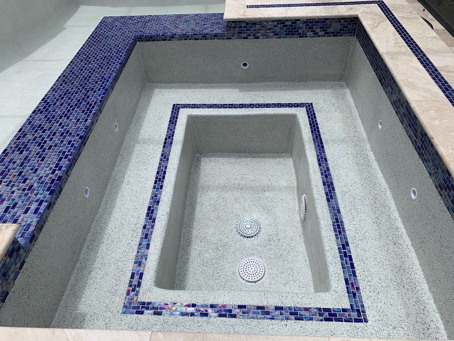 Rectangular concrete pool with blue mosaic tile borders and a smaller inner basin, viewed from above