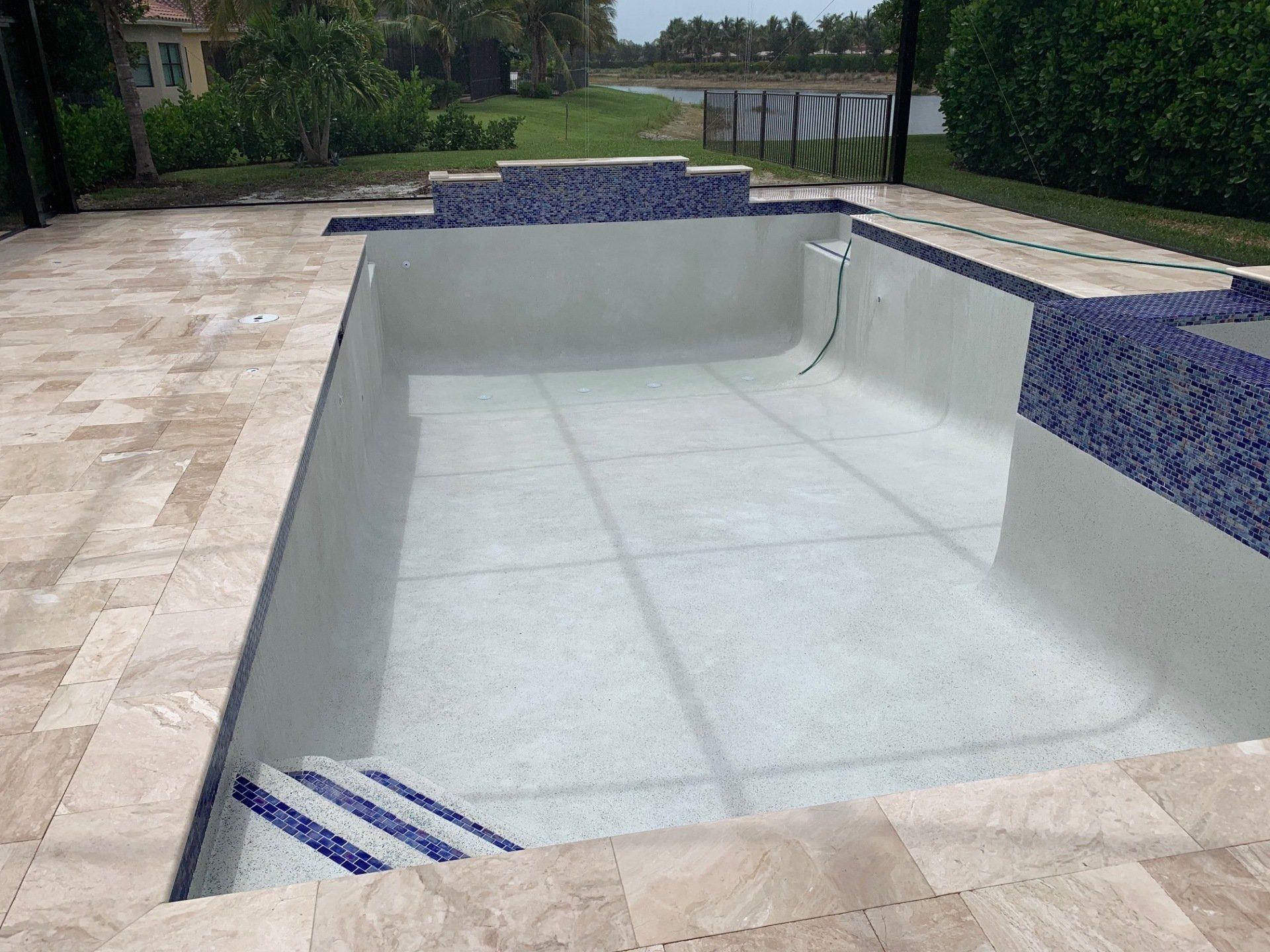 Empty swimming pool with white interior, blue tile trim, and stone deck outdoors