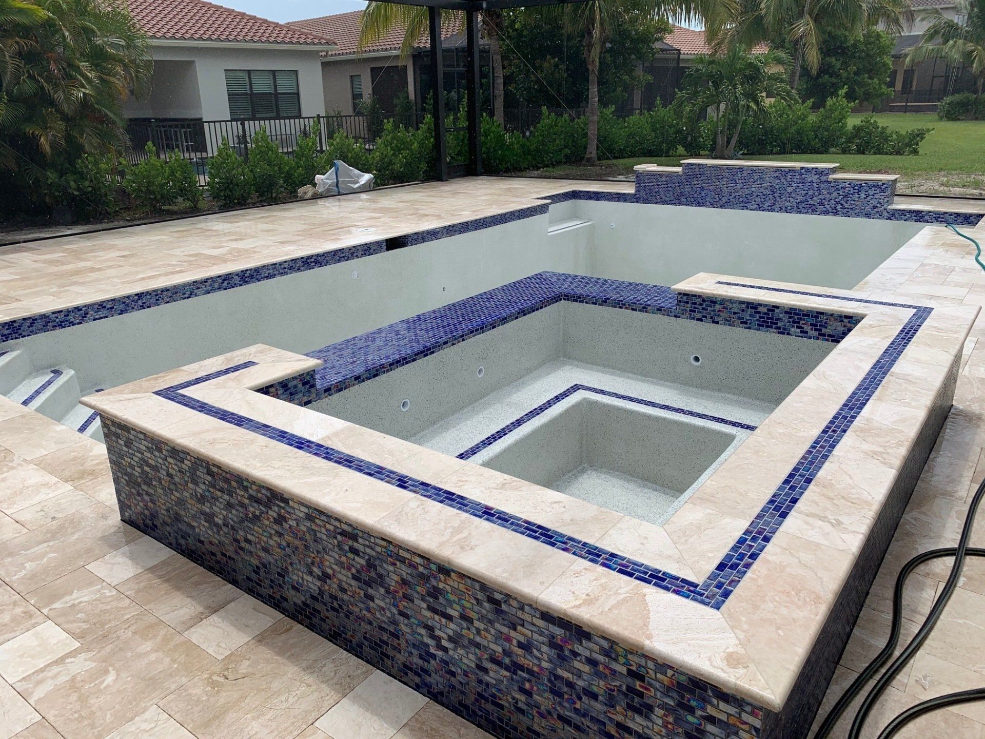 Empty backyard pool with a raised square spa, blue tile, and beige stone deck.