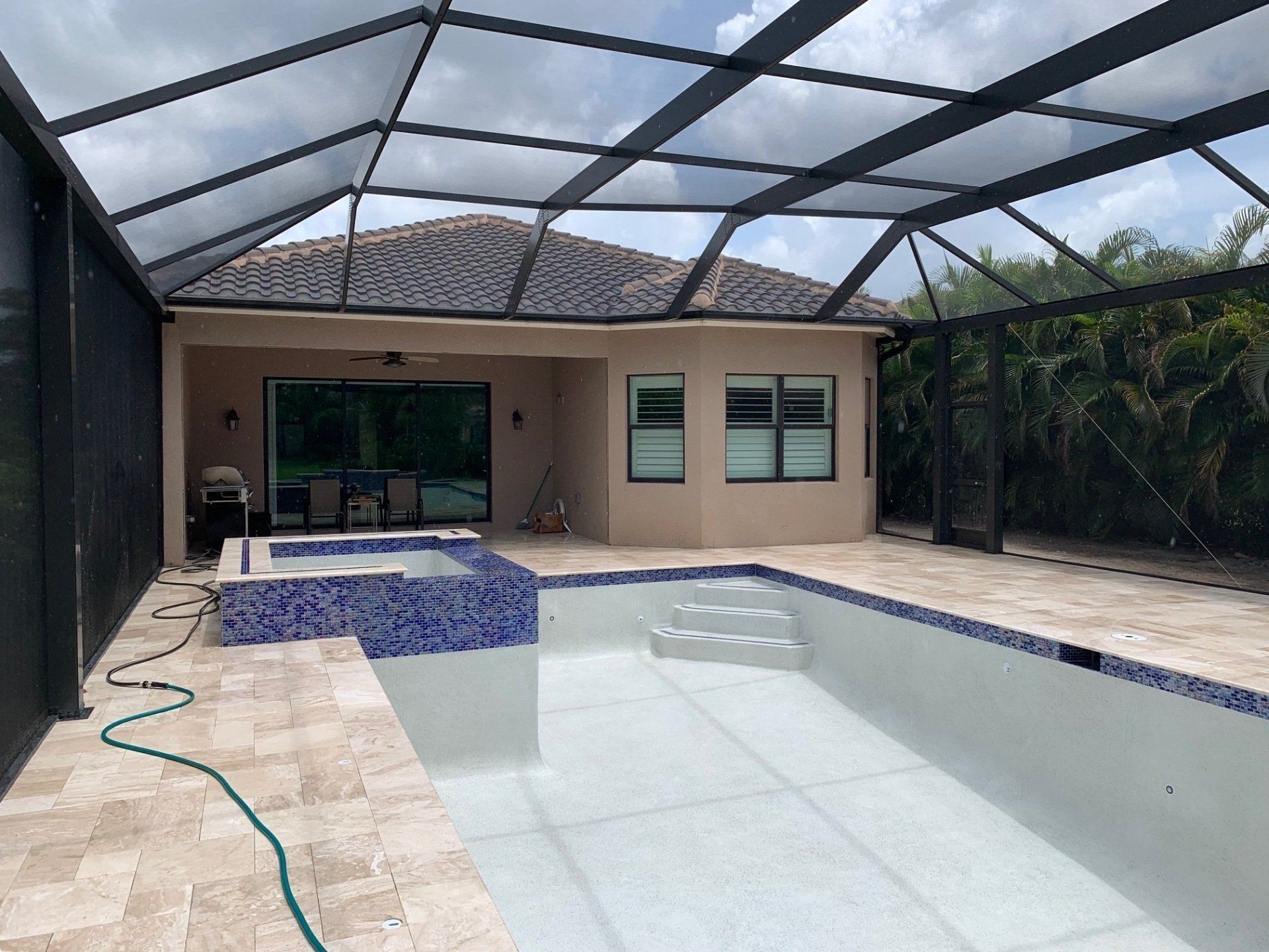 Covered backyard pool with tiled patio, screened enclosure, and a house in the background.