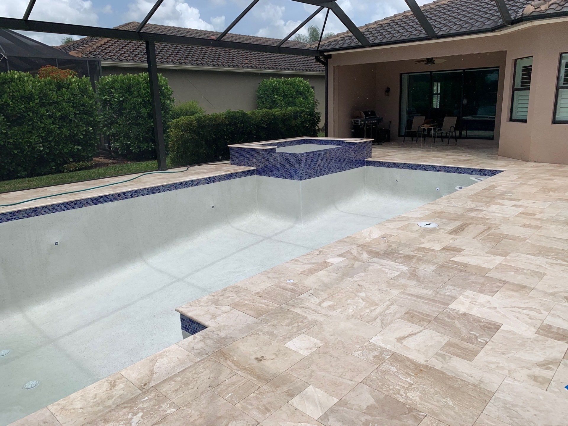 Empty backyard swimming pool with blue tile trim and a covered patio nearby