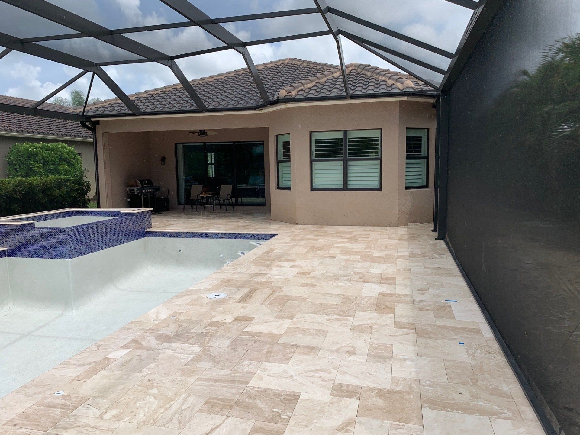 Covered backyard pool patio with beige tile, screened enclosure, and house sliding doors