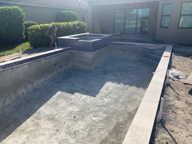 Empty concrete swimming pool under construction beside a modern house, with a worker nearby