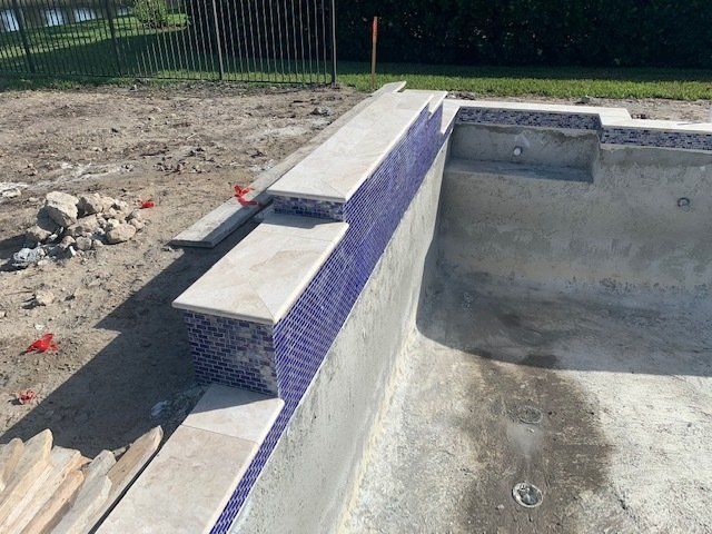 Empty backyard pool under construction with concrete walls, blue tile trim, and dirt surrounding it