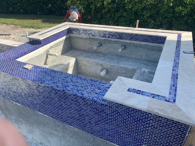 Empty tiled swimming pool under construction with blue mosaic border and concrete interior
