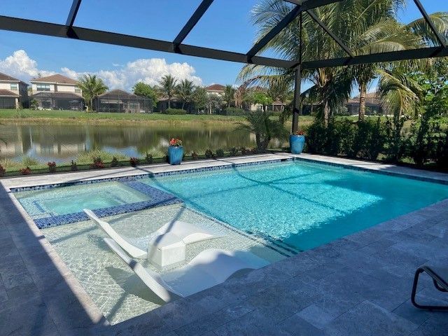 Screened backyard pool with blue water, two lounge chairs, and a lake view beyond the patio