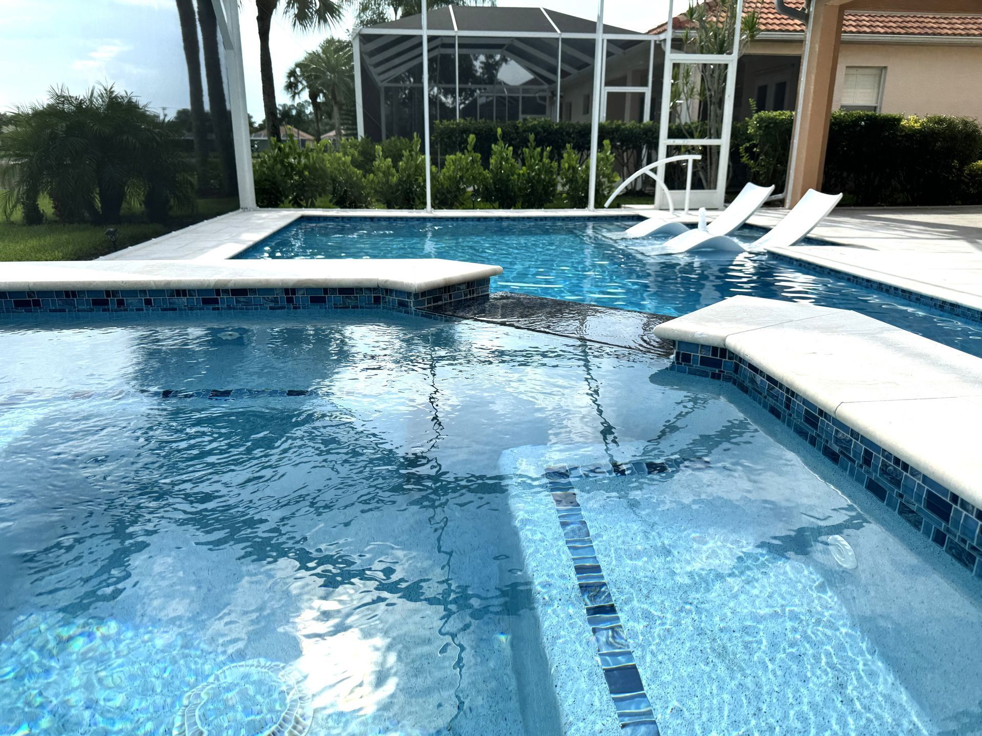 Blue swimming pool with white lounge chairs and a screened patio in the background