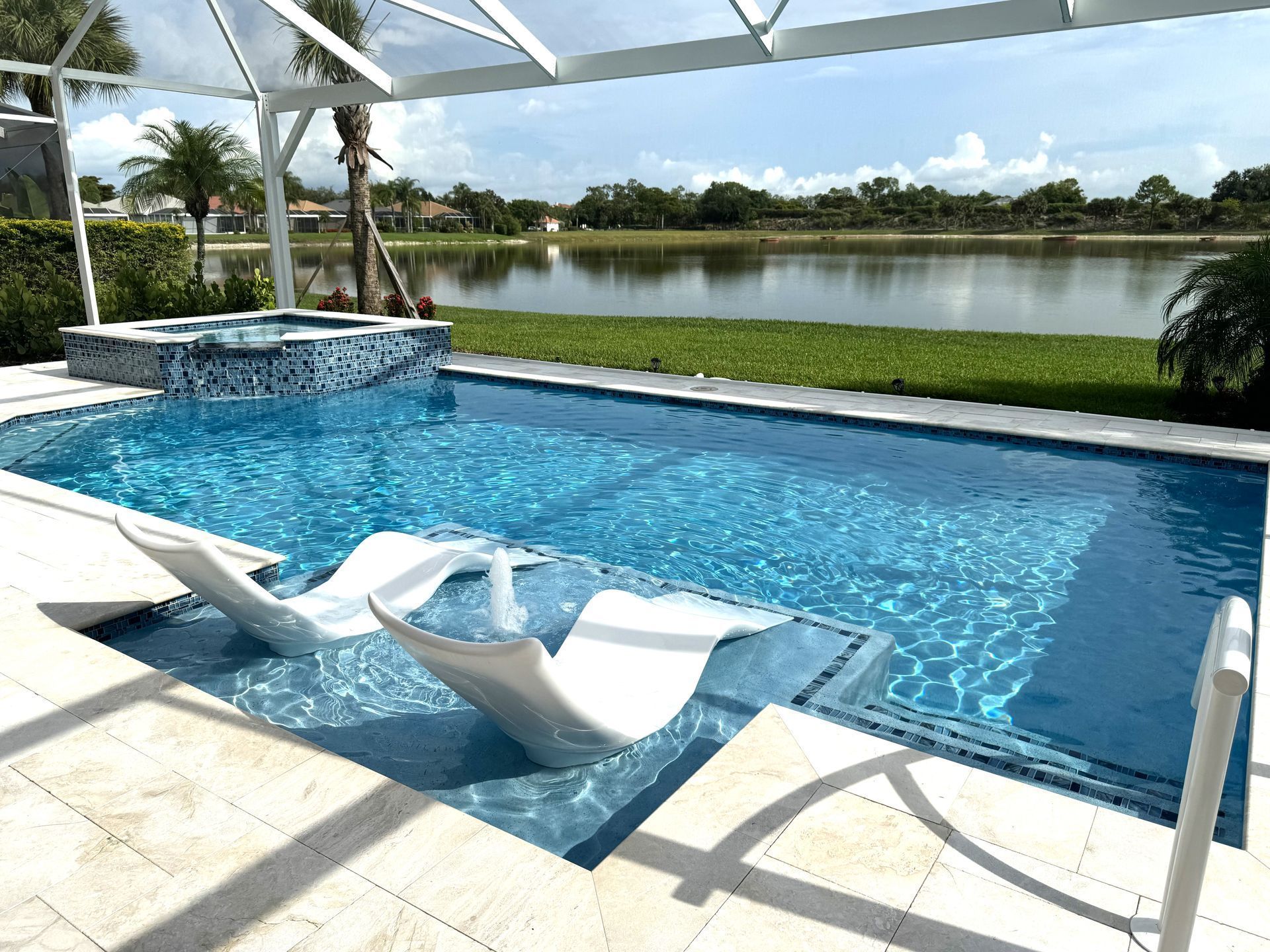 Modern backyard pool with white lounge chairs, blue water, and a lake view under a partly cloudy sky