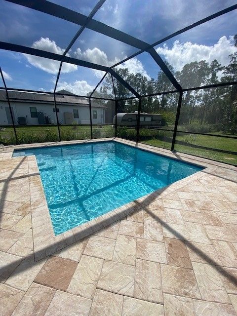 Screened backyard pool with blue water and beige stone patio under a black metal enclosure